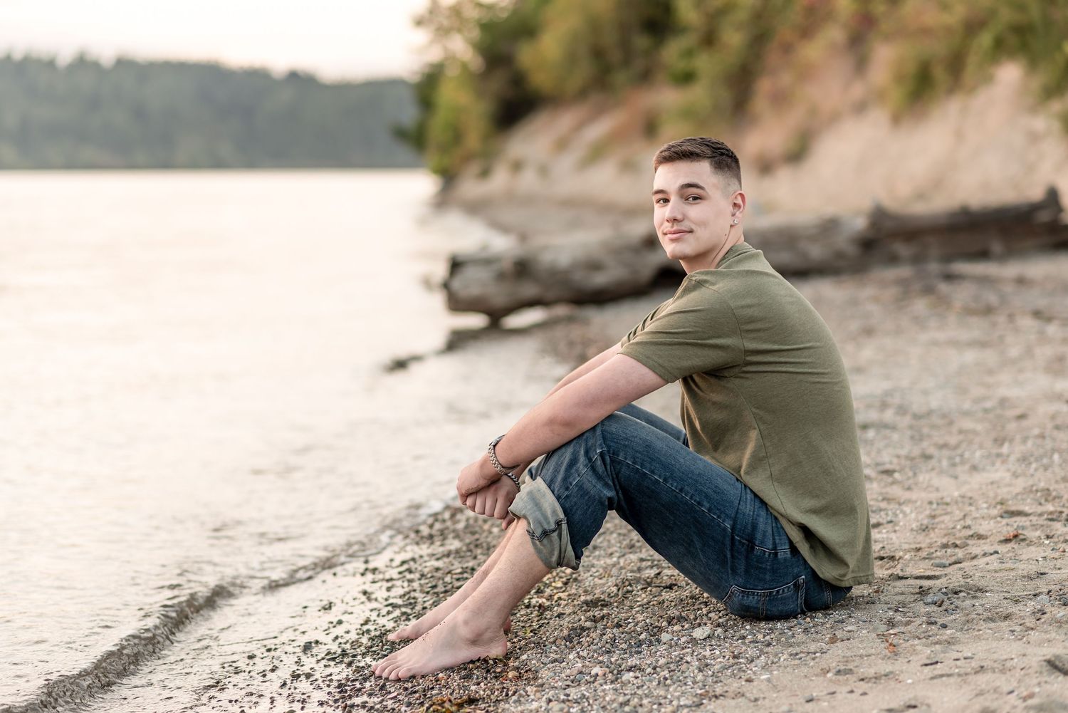 A relaxed shoreline scene featuring someone sitting on a rocky beach at sunset.