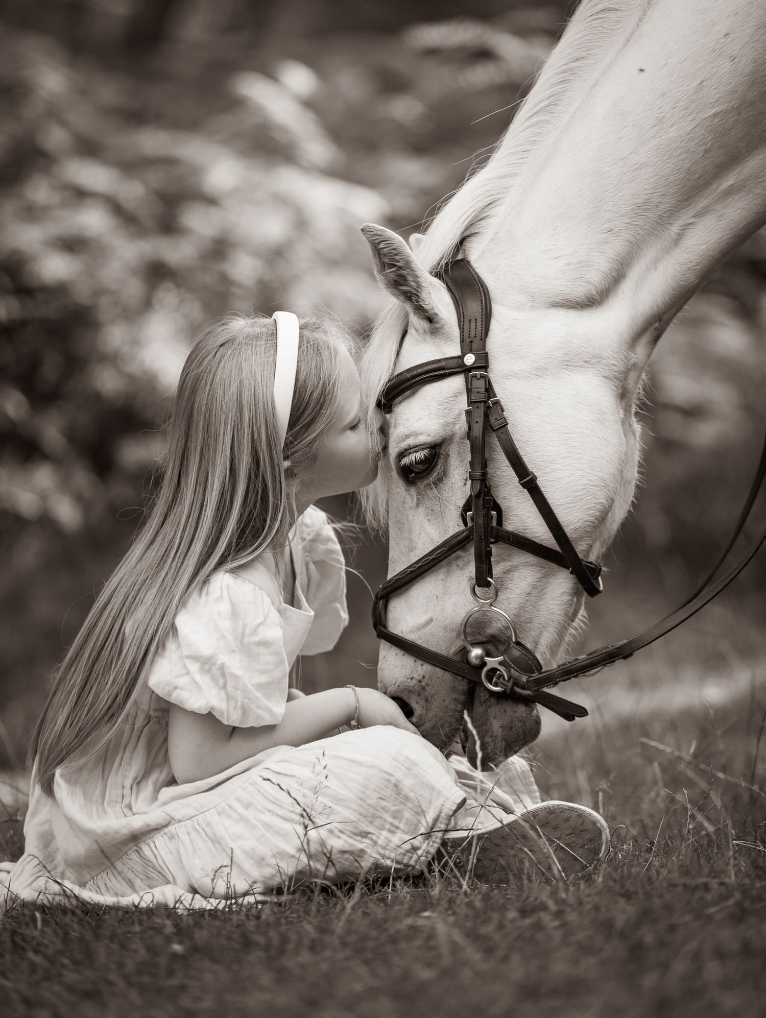 Young girl in denim overalls embraces a palomino horse in a sun-dappled forest setting.