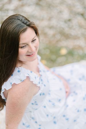 Smiling brunette woman in white floral dress looking down, photographed from above in soft natural light.