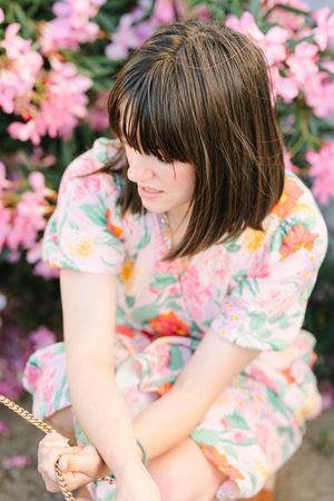 A dreamy portrait among pink flowering bushes wearing a floral print dress.