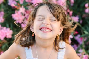 Child smiling brightly in natural light with pink flowers in background.