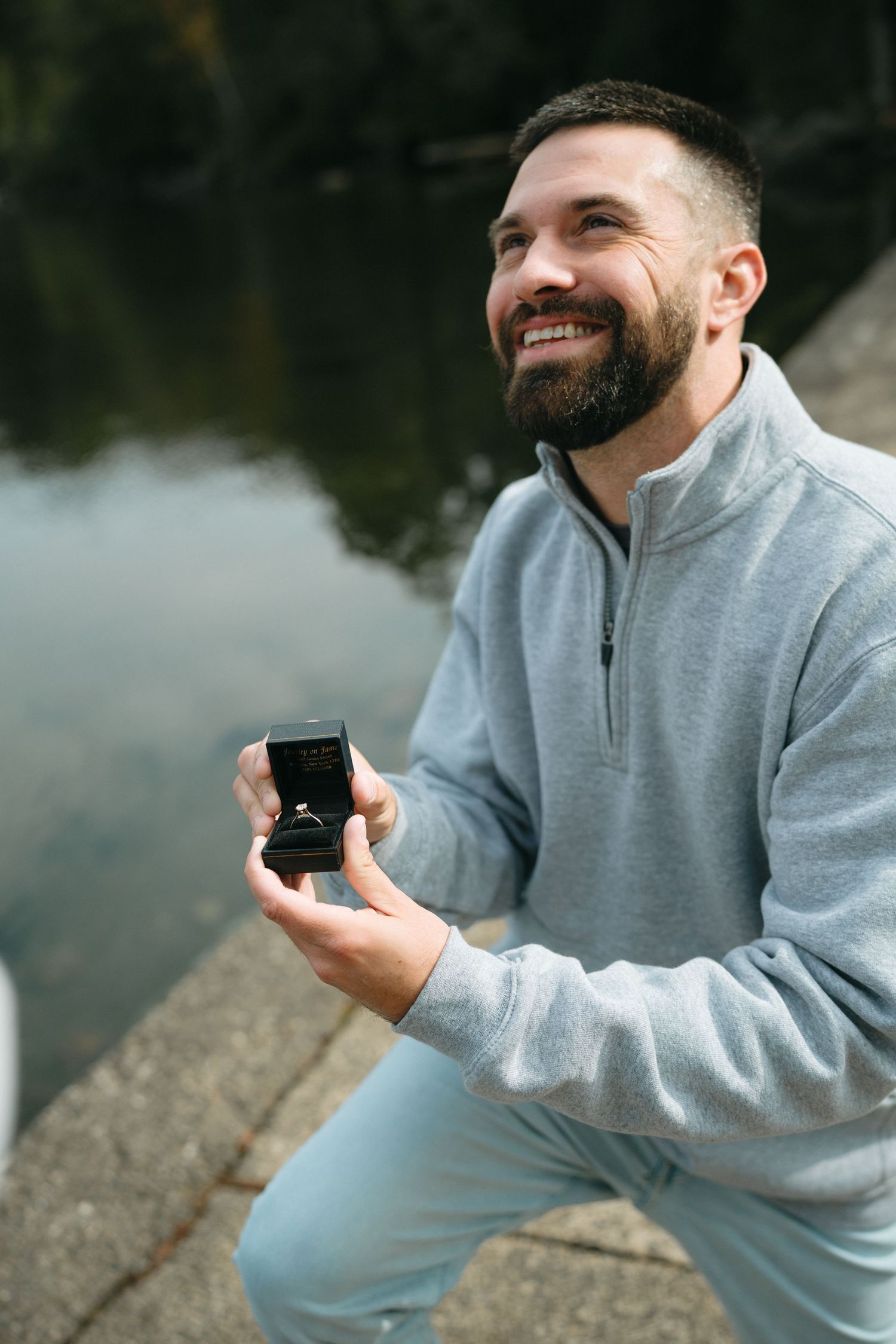 A person in a gray sweatshirt holds a small box while smiling outdoors on a misty day.