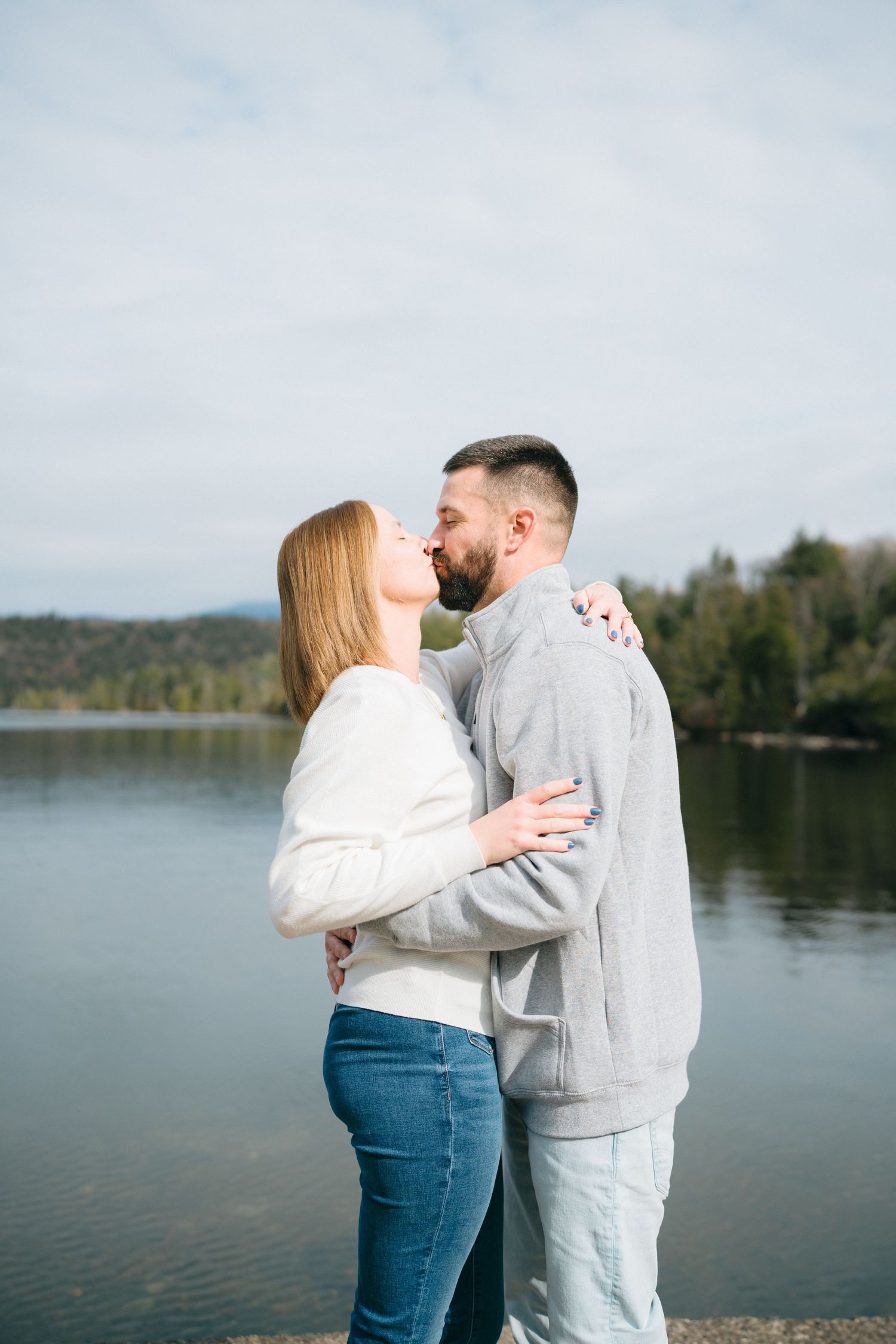 A romantic lakeside moment between two people in casual attire against a serene water backdrop.