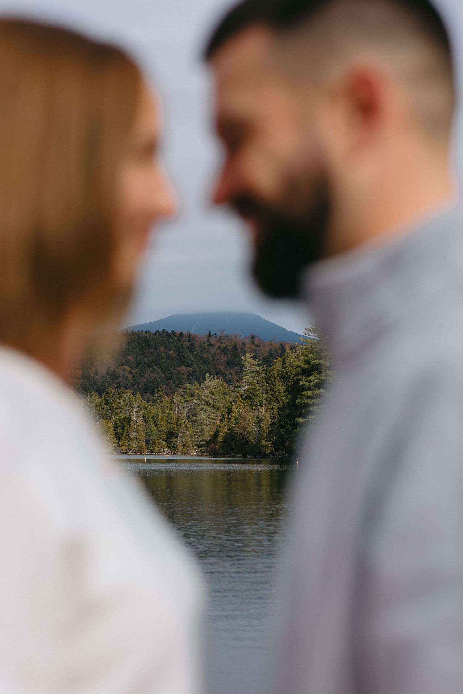 A serene lakeside scene with pine-covered mountains in the background and people in white and gray clothing in the foreground.