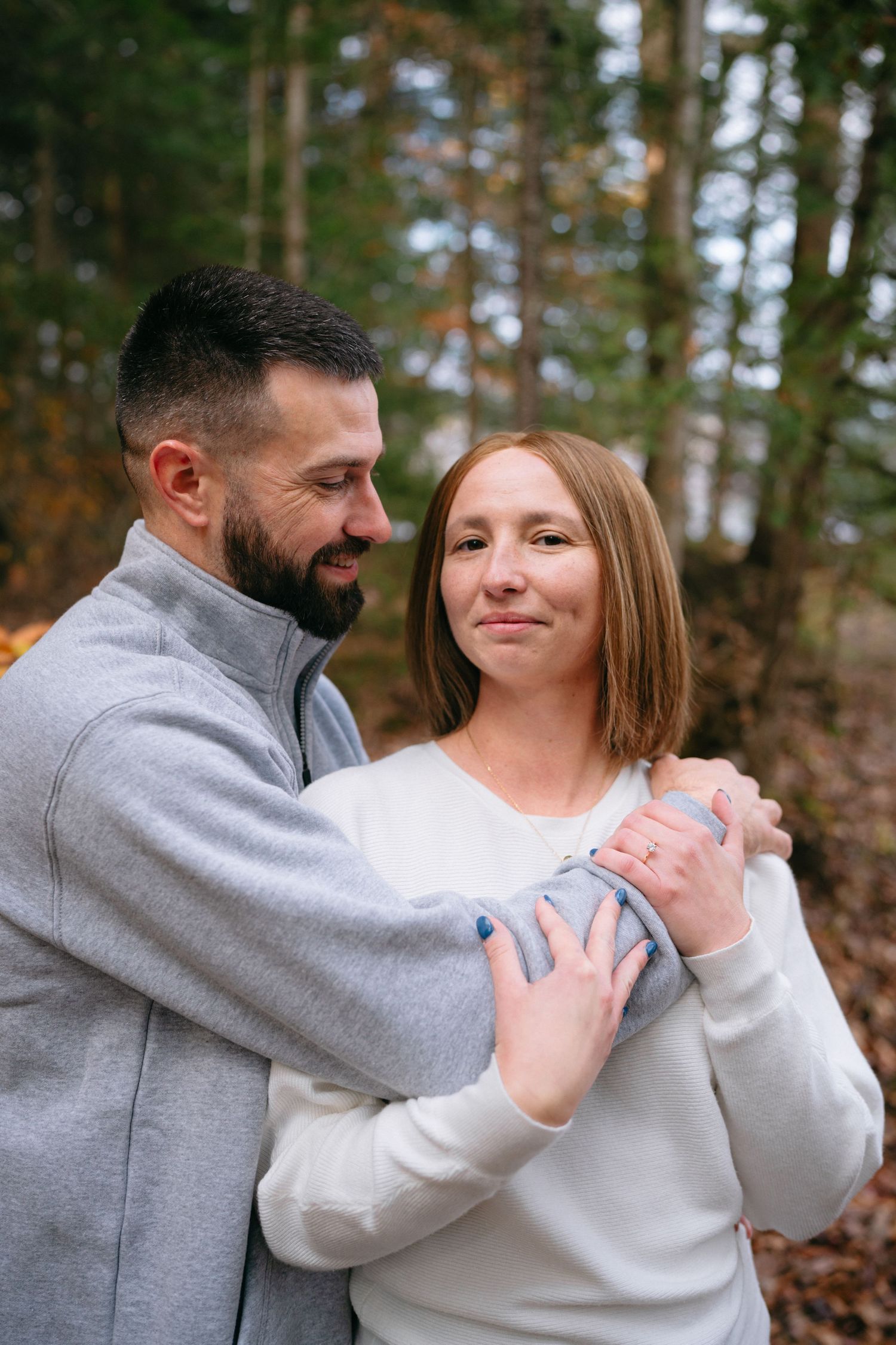 A couple embraces and laughs together in a wooded setting during autumn.
