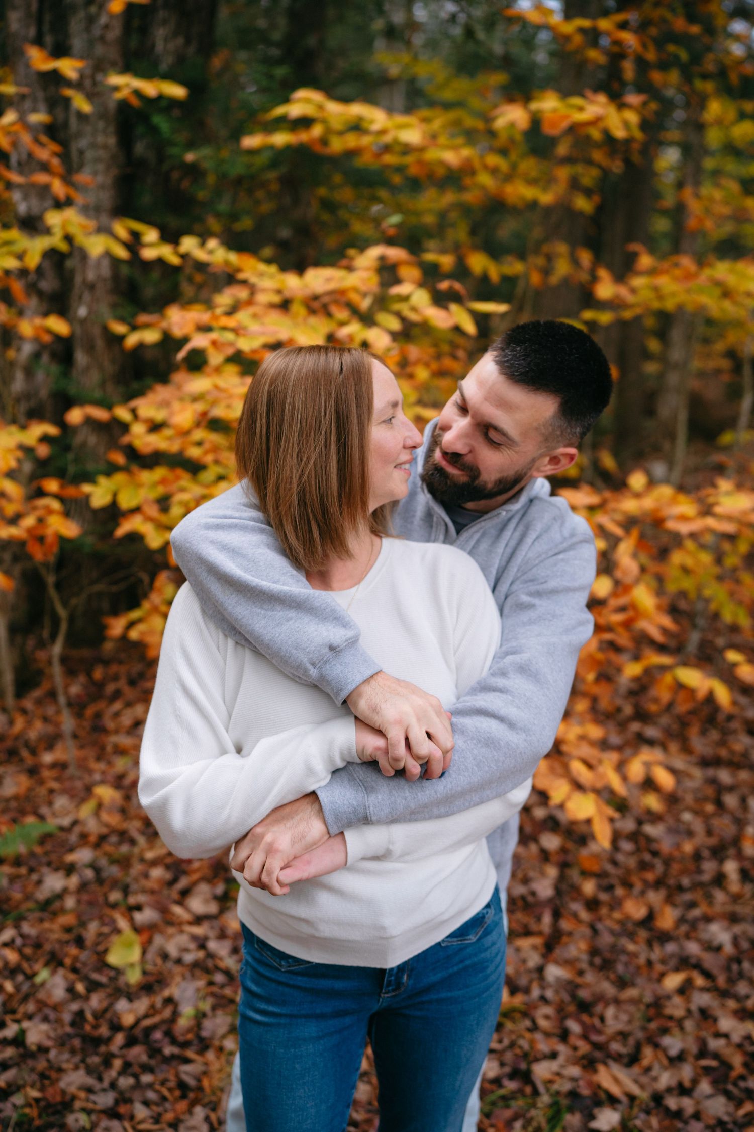 Two people share an intimate moment surrounded by vibrant fall colors and pine trees.