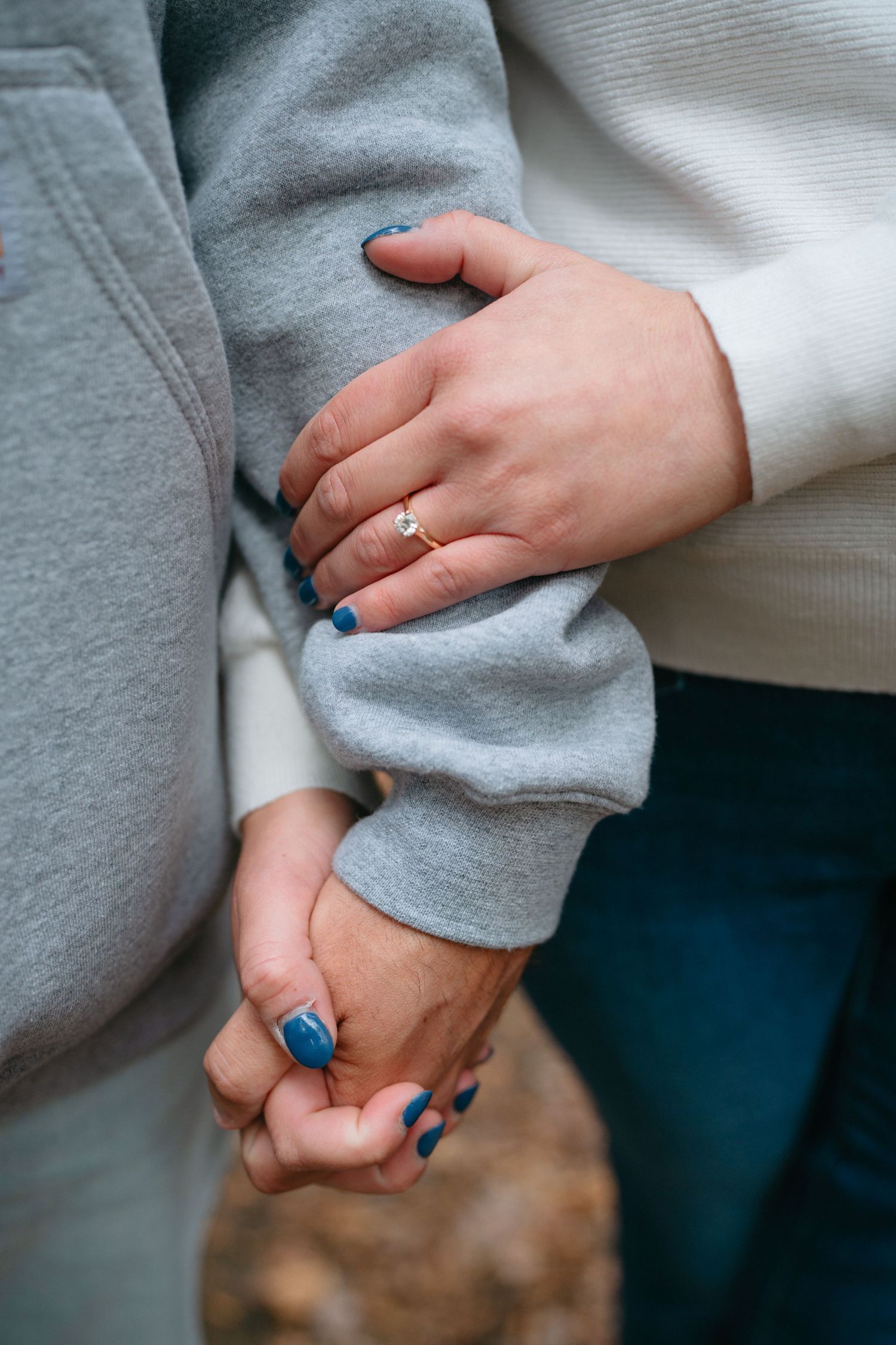 Close-up of hands wearing rings touching tenderly against grey and white clothing.