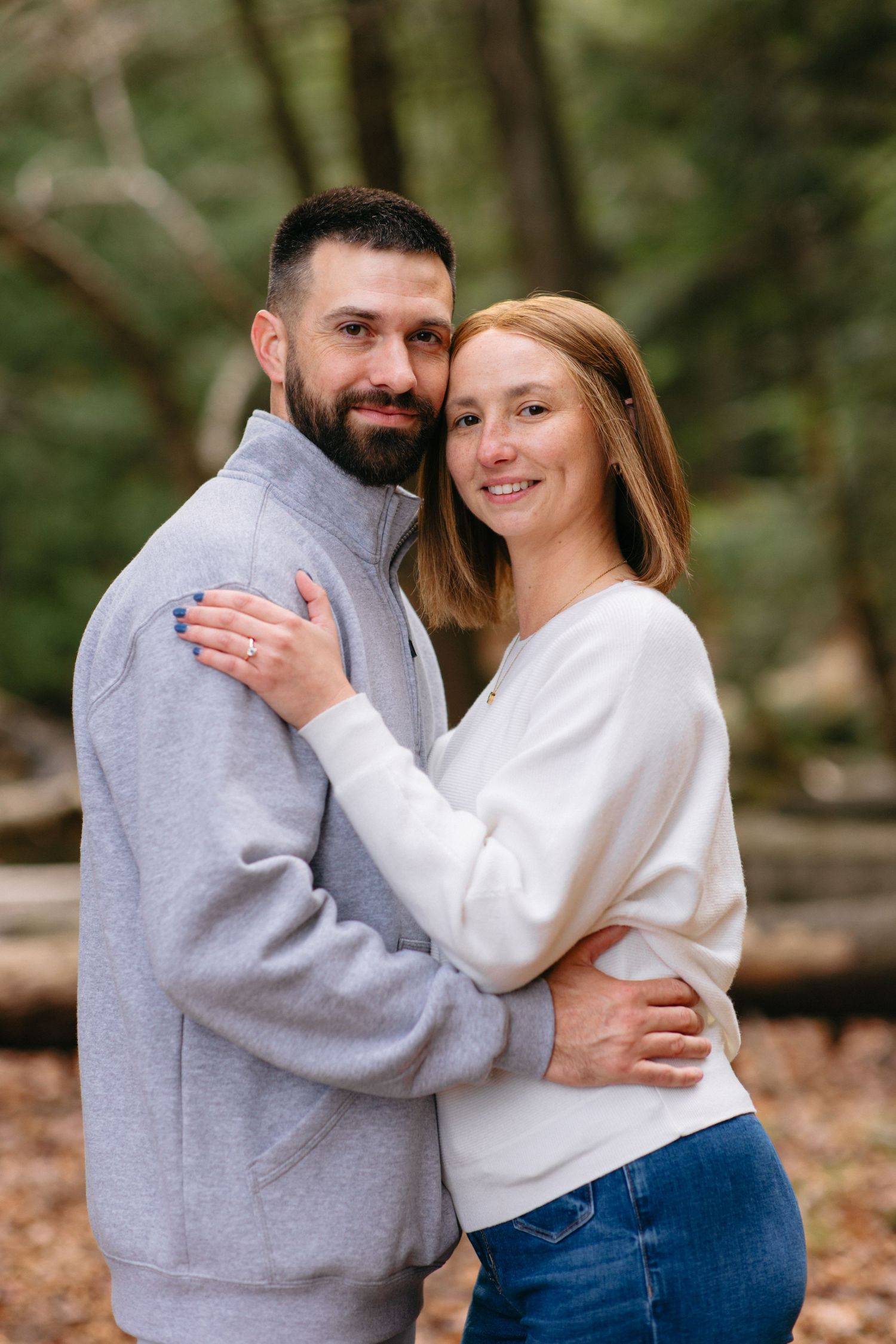 Two people share an intimate embrace while wearing casual clothing in a natural outdoor setting.