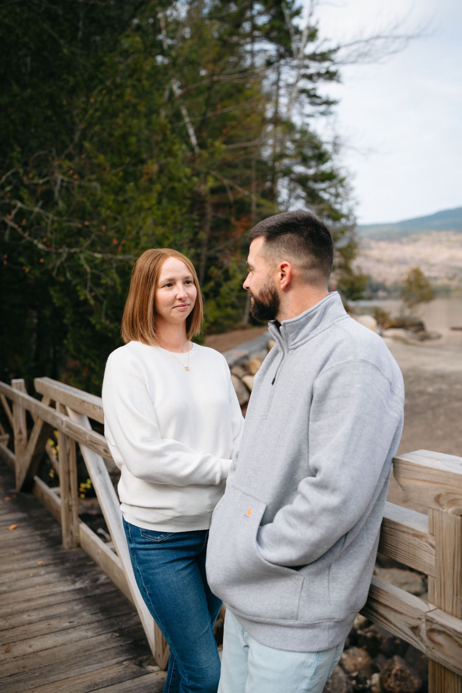 A couple shares joyful moments on a wooden bridge surrounded by autumn scenery.