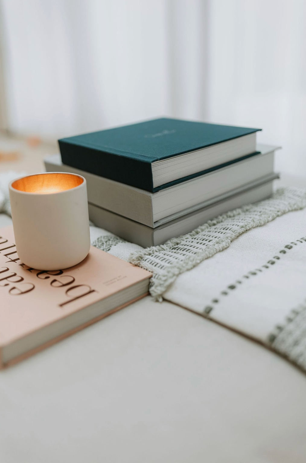 A minimalist composition with hardcover books and a glowing white candle holder on a textured surface.