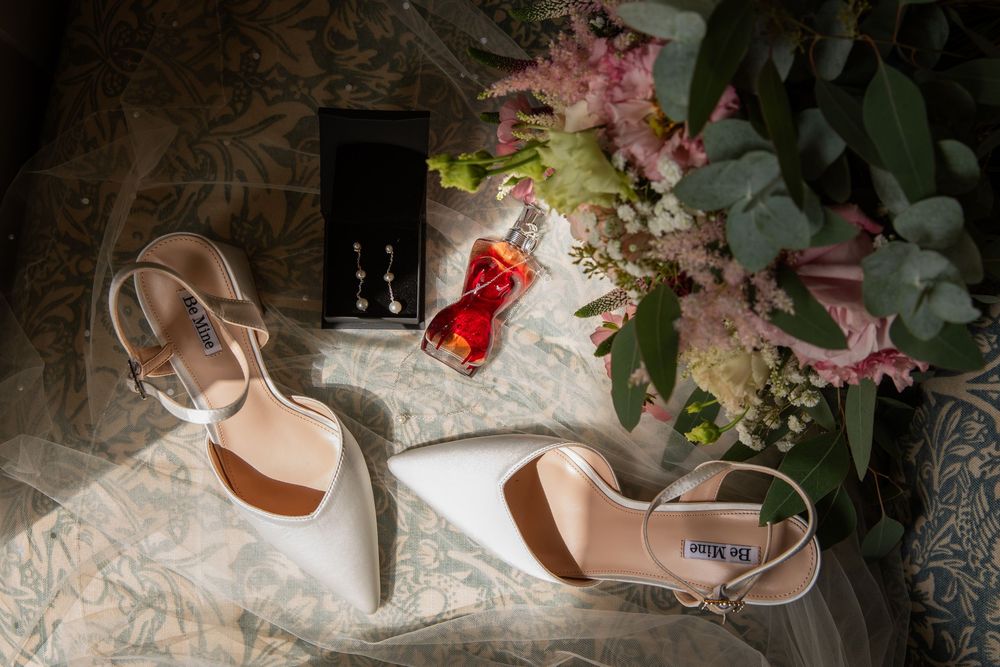 Wedding accessories including pink flowers and elegant bridal shoes arranged on lace fabric.