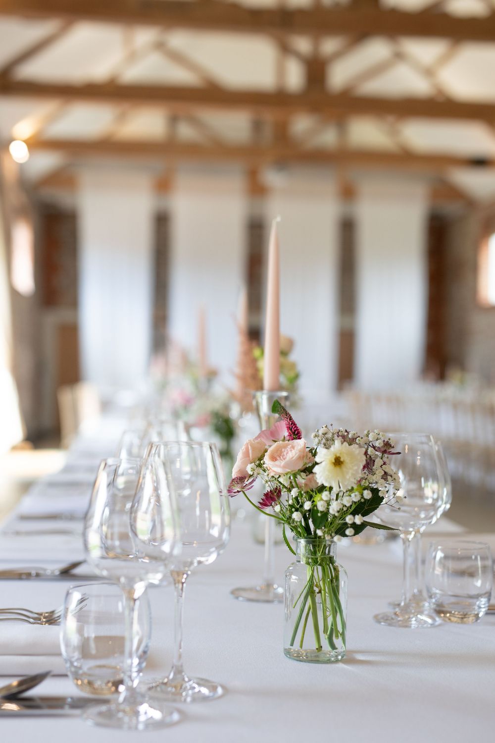 Elegant wedding reception table settings with delicate floral centerpieces in glass vases and crystal wine glasses.