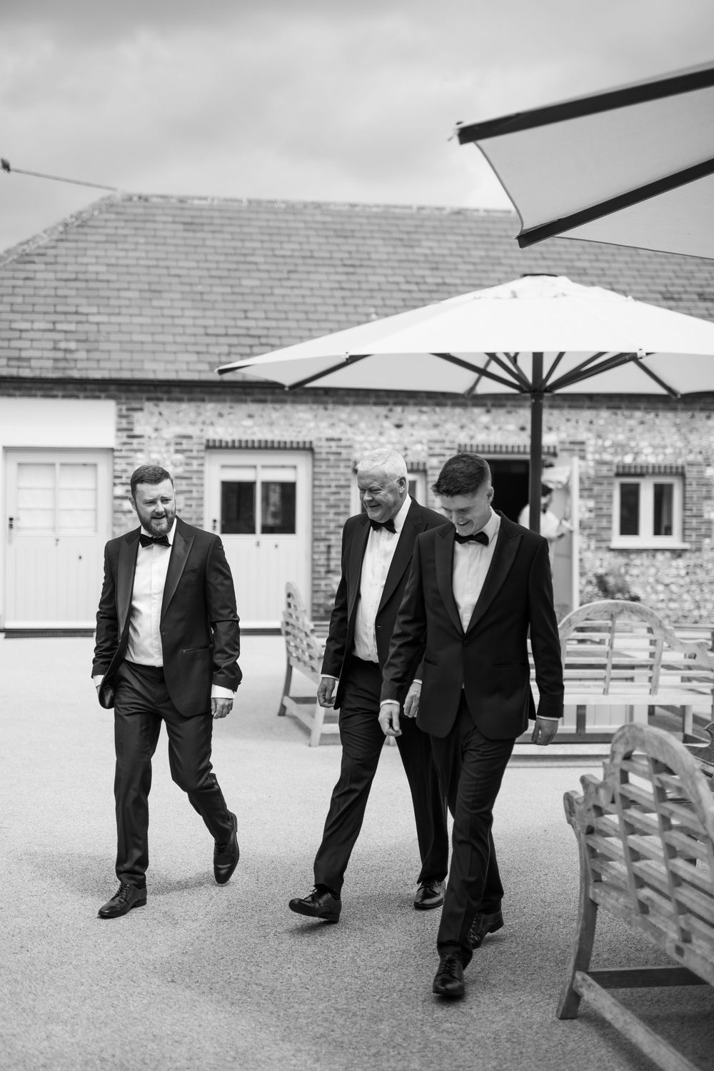 A sequence of black and white photos showing groomsmen walking together outside a brick building in formal attire.