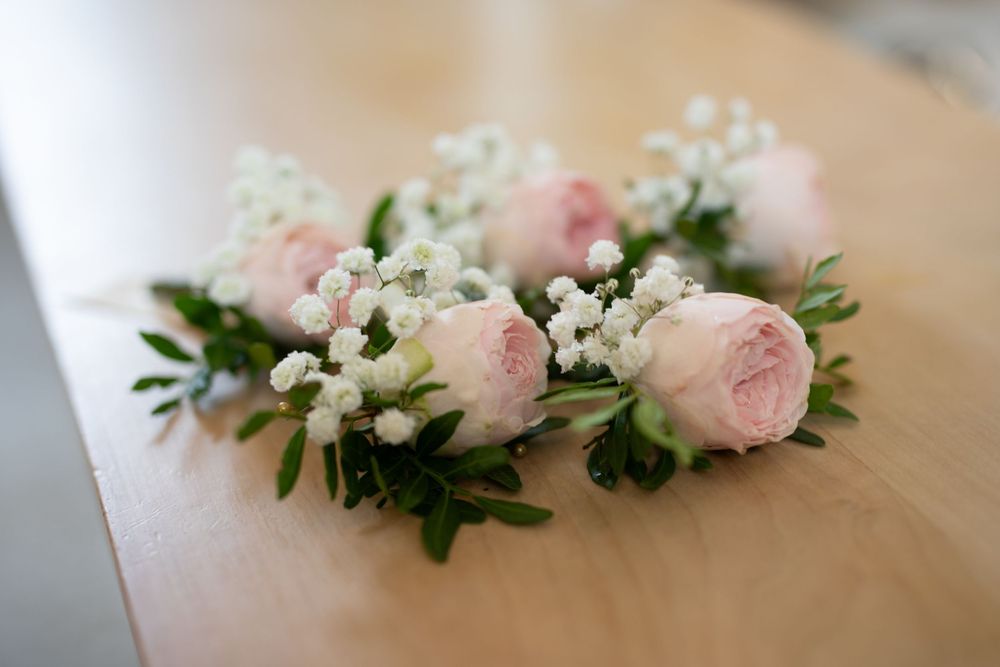 A delicate floral arrangement with pink roses and white flowers adorns a wooden surface.