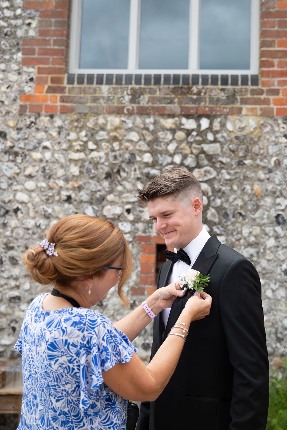 Wedding preparation scene against stone wall with person pinning boutonniere on formal suit.