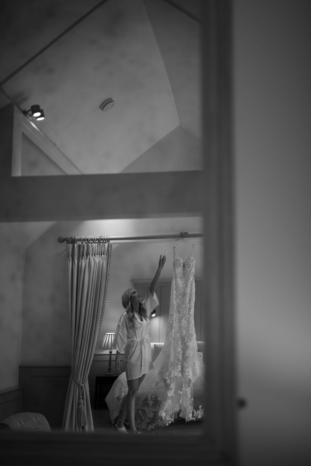 Wedding dress hanging in a bridal suite with soft lighting and curtains.