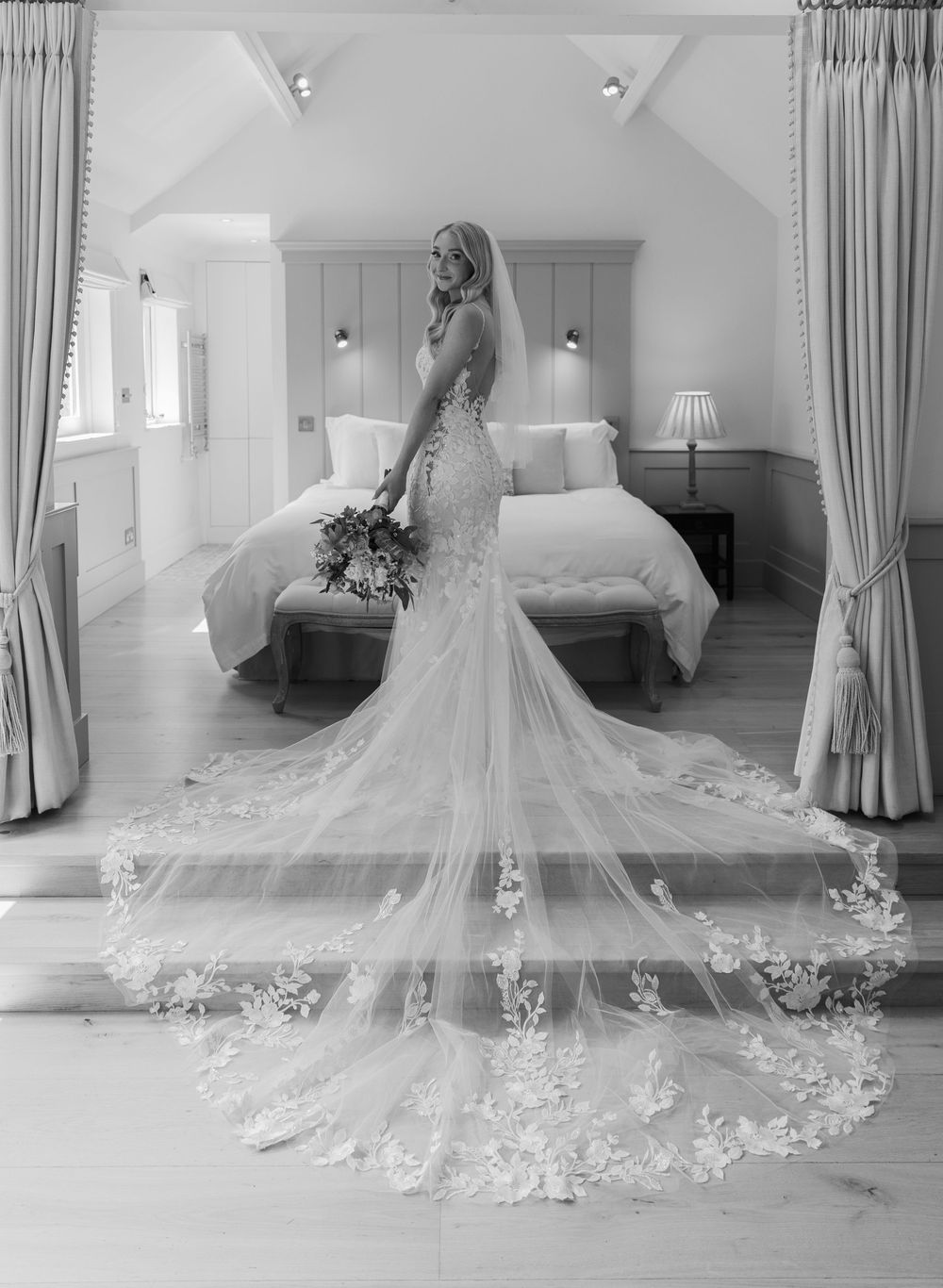 Elegant lace wedding dress with cathedral length veil laid out on floor in bridal suite.