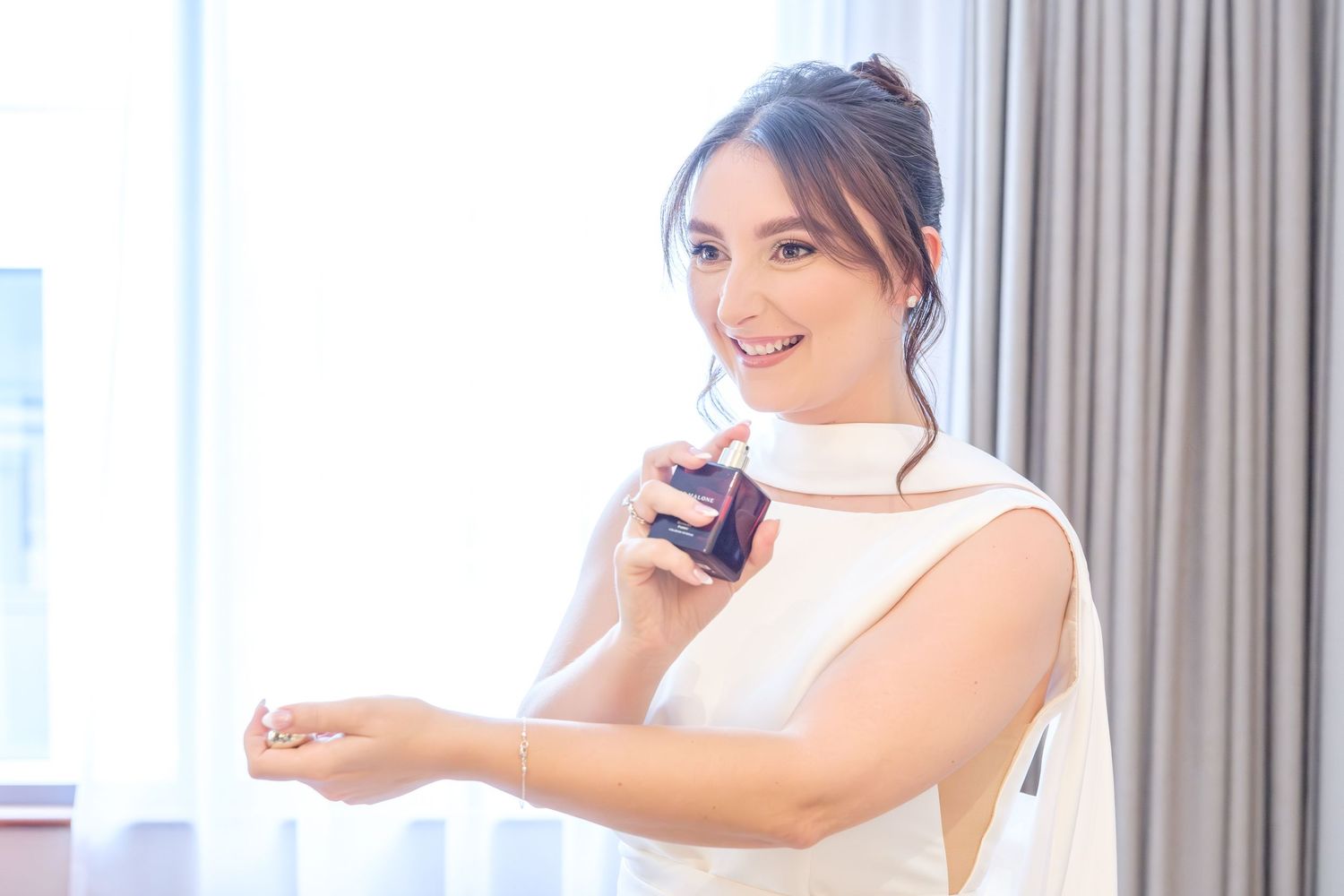 A person in white dress uses a handheld steamer to remove wrinkles from clothing hanging in a bright room.