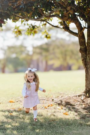 Child in white dress playing under trees on autumn day.