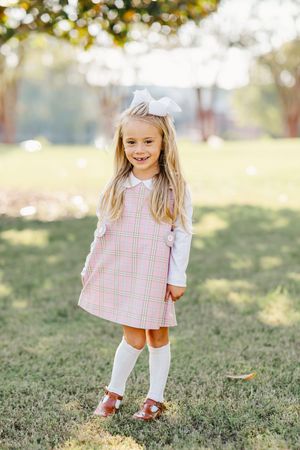 Young child wearing pink plaid dress and white knee socks playing outdoors on grass in sunlight.