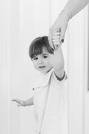 Black and white portrait of child peeking through white curtains.