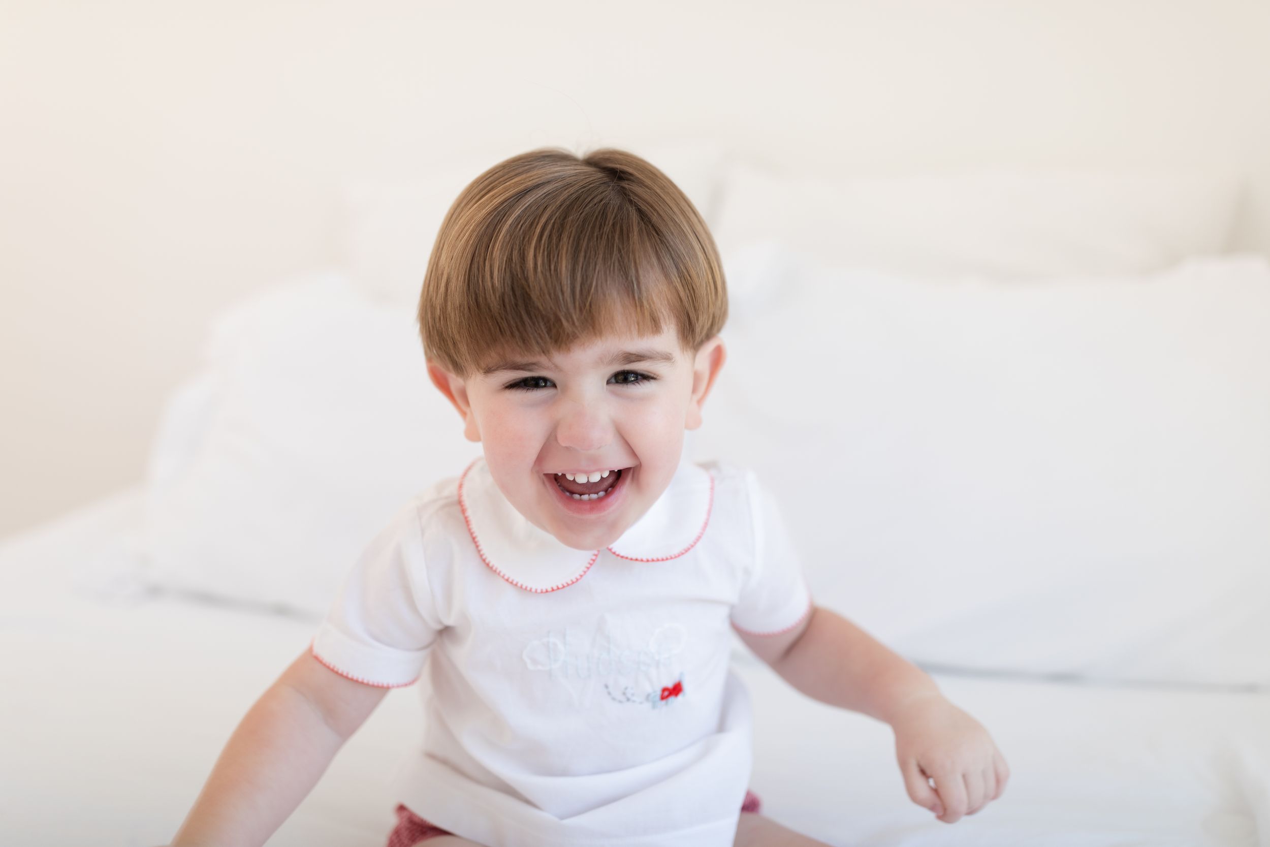 Child in white collared shirt smiling and playing on light background.