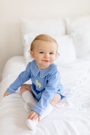 Baby in light blue collared outfit lying on white bedding.
