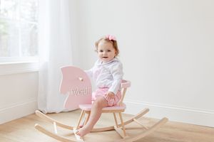 Pink wooden rocking chair against white wall in minimalist nursery setting.