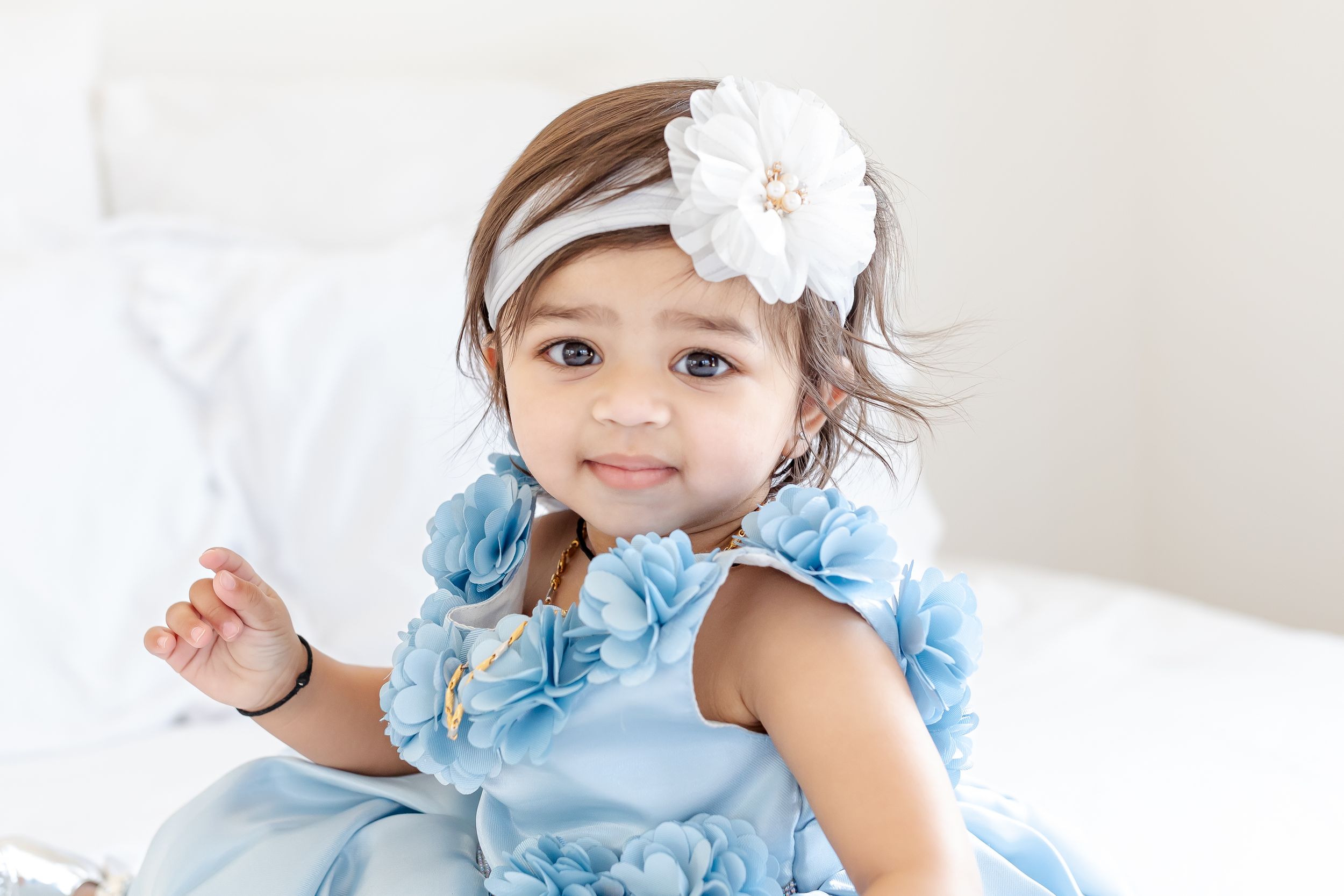 Baby wearing a light blue dress with ruffles and white bow headband.
