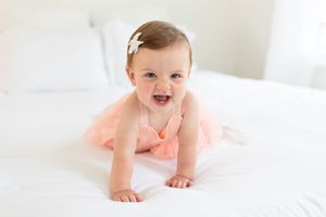 Baby in white outfit crawling on soft white bedding.