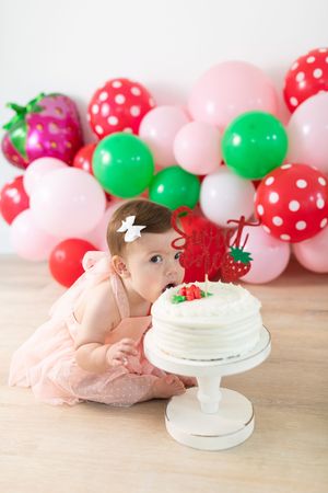 Festive cake setup with strawberry decorations and pink and red polka dot balloons.