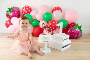 Colorful balloon garland with red, green, and pink balloons beside a white cake stand.