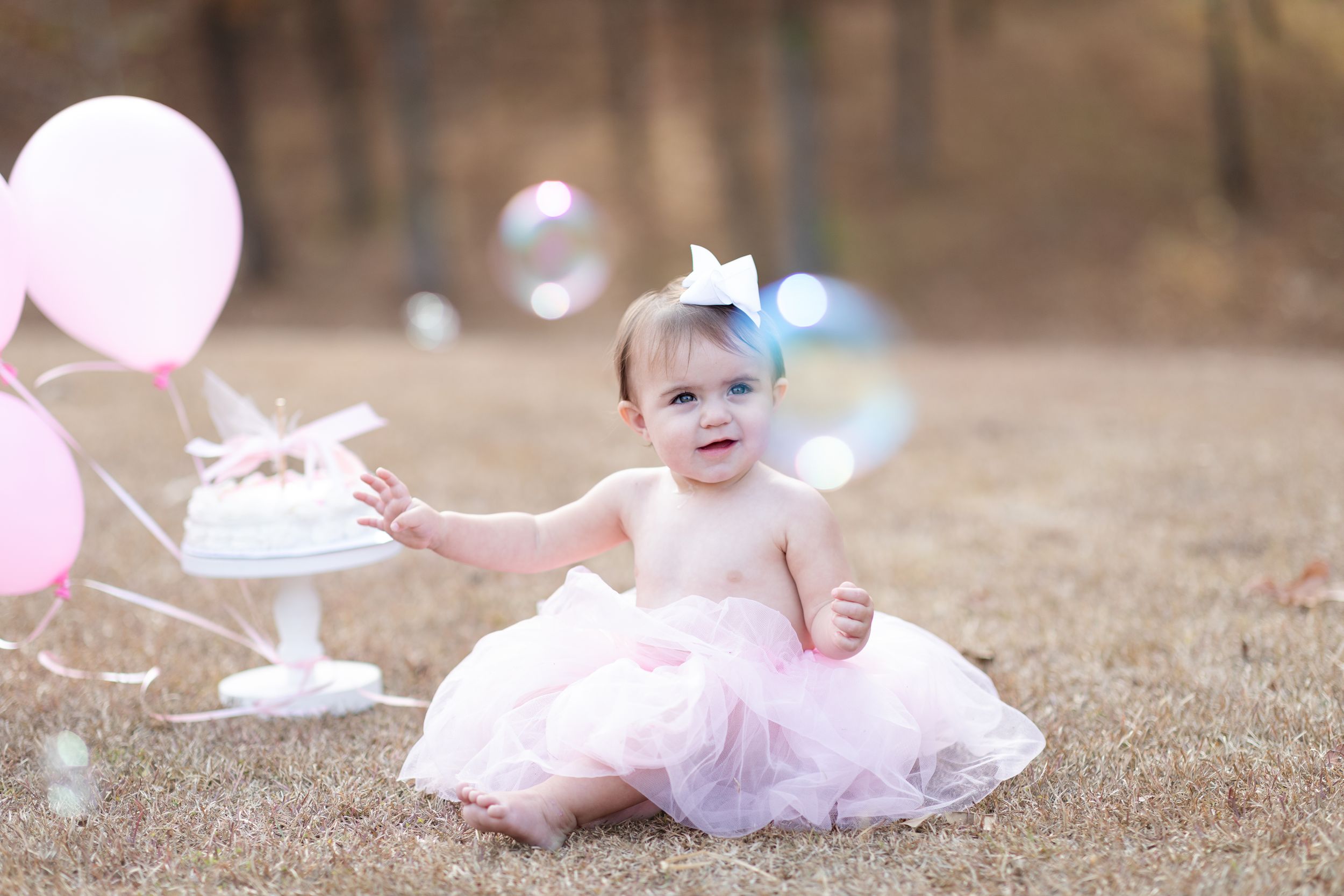 Outdoor photography session with bubbles and pink tulle dress on sandy ground.