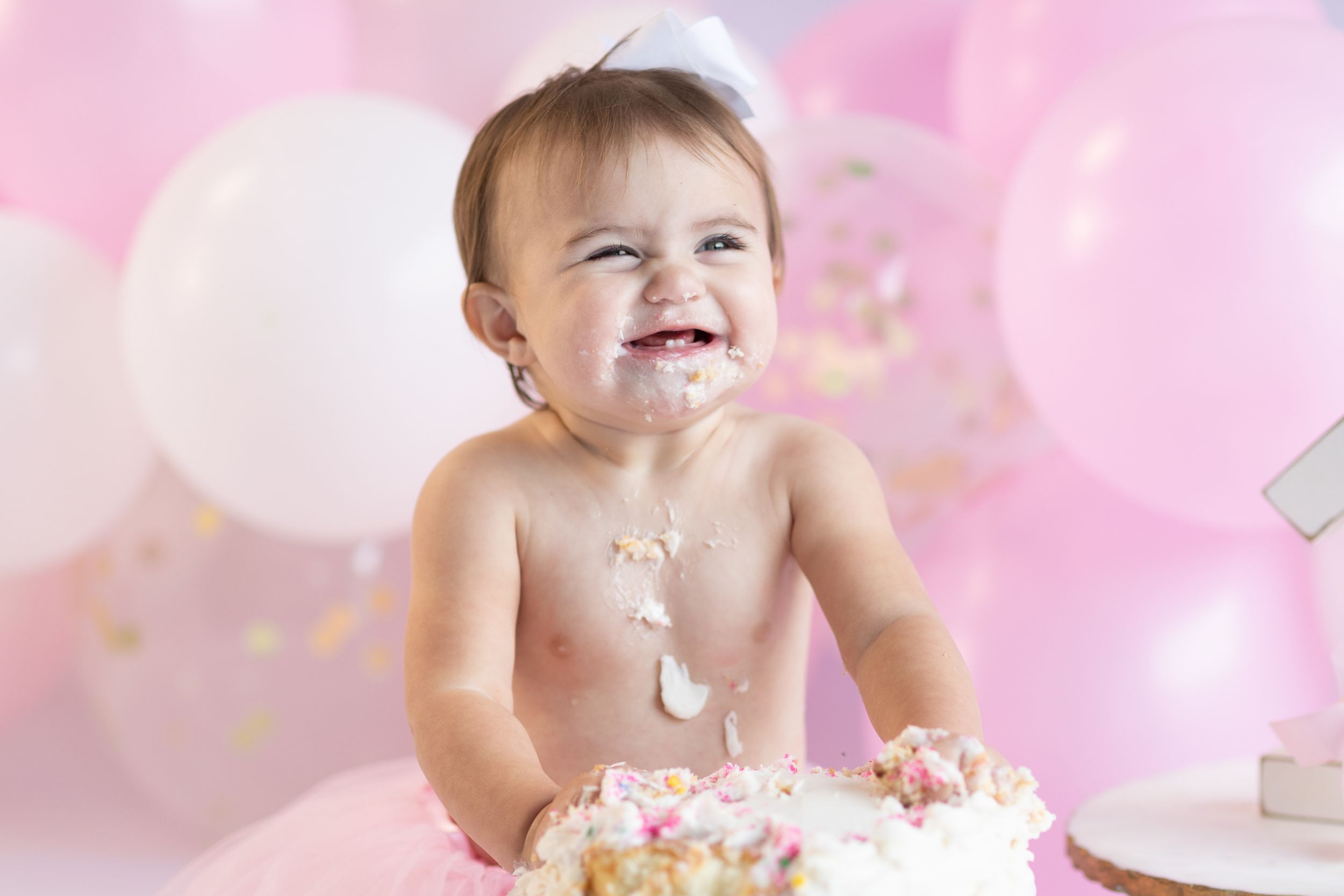 First birthday cake smash photography session with pink balloons and white decorations.