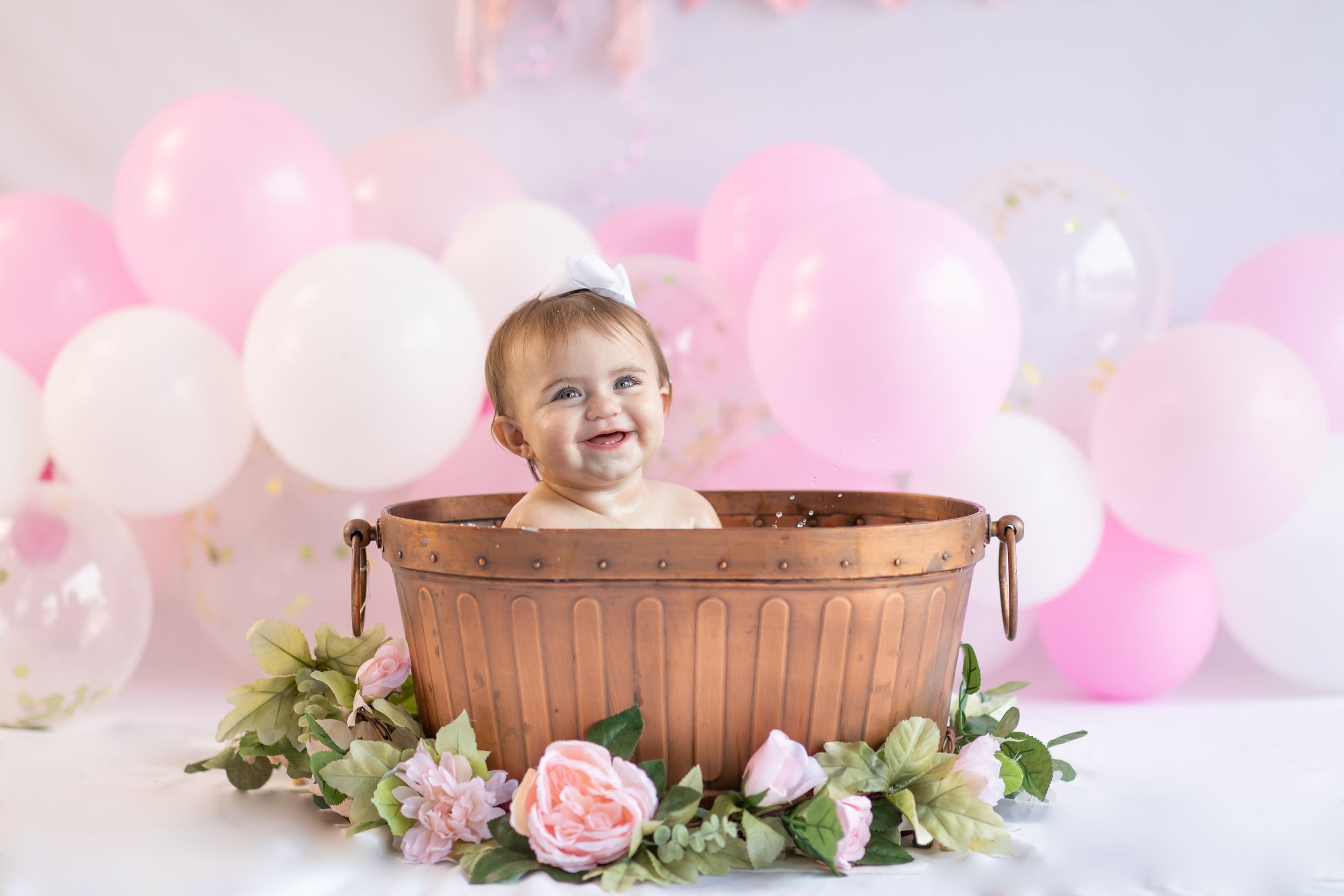 Delicate newborn photo setup with pink balloons and wooden basket against soft lighting.