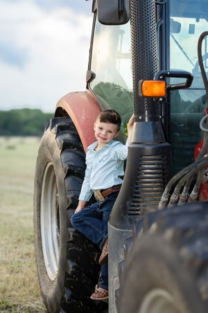 Small child sits in large tractor against rural farmland backdrop.