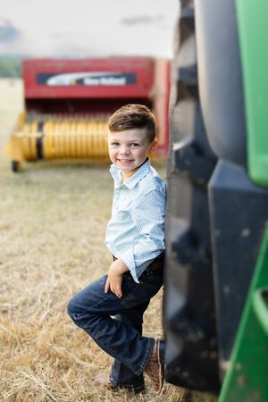 Young child poses beside green tractor in countryside setting.