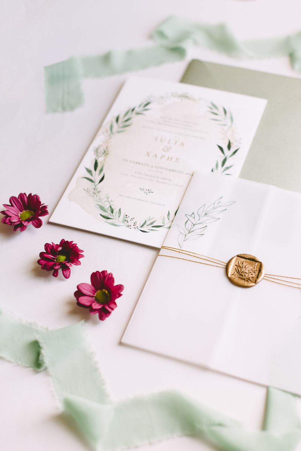 Elegant wedding invitation suite with pink flowers and gold wax seal displayed on white background with sage green accents.