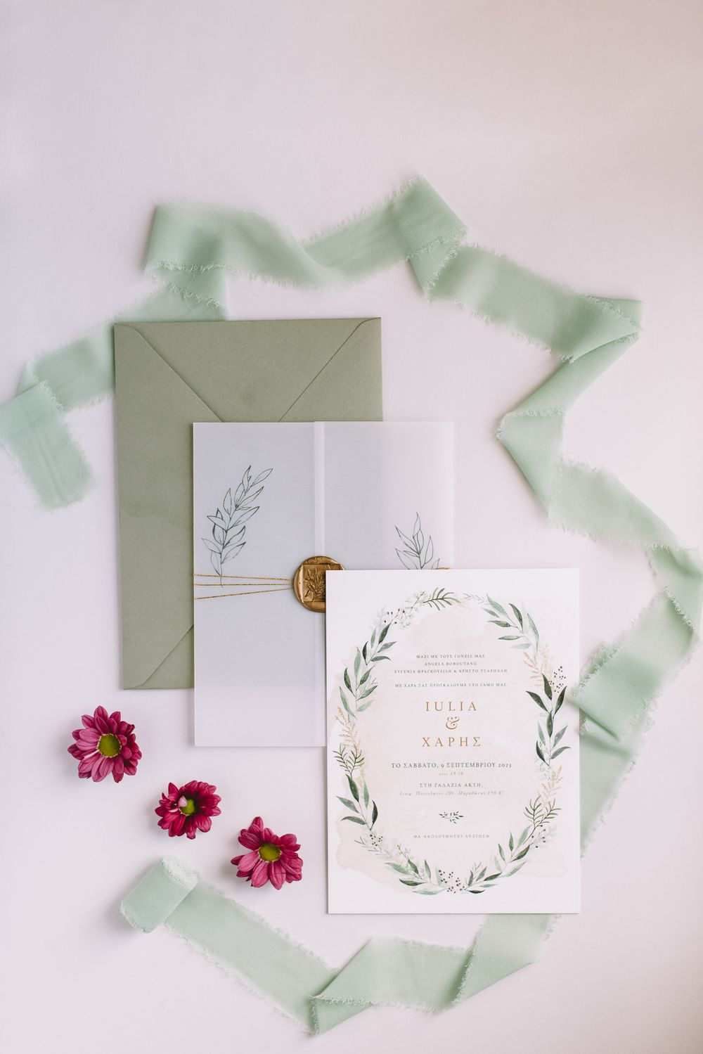 Elegant wedding invitation suite with sage green envelope, floral design, pink flowers and mint ribbon on white background.