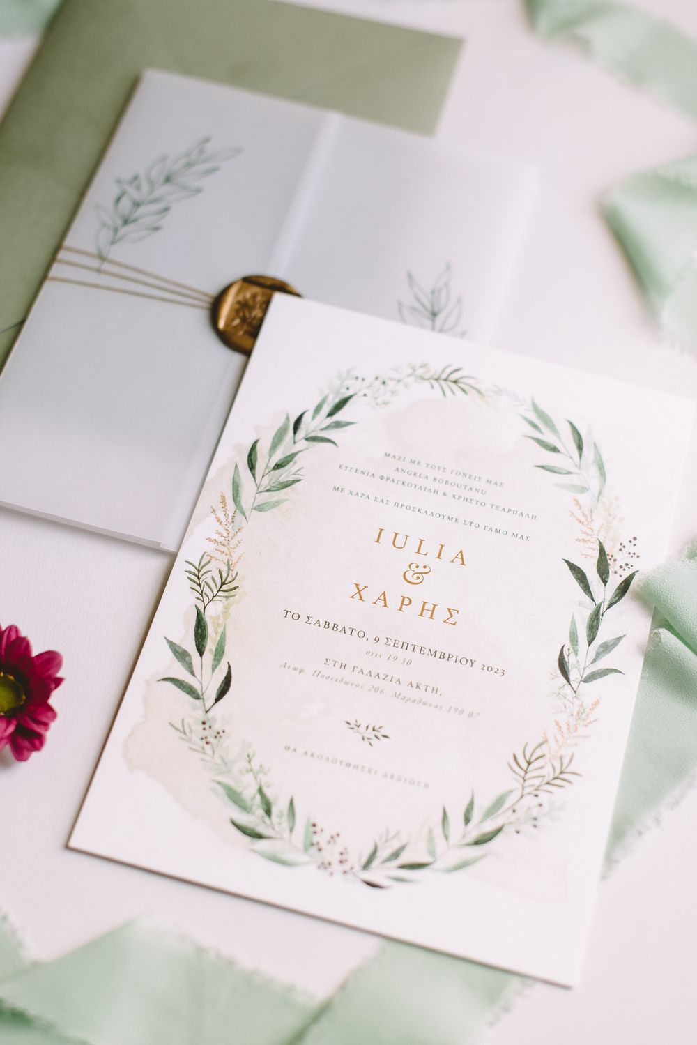 Elegant white wedding invitations with delicate green watercolor olive leaves and gold foil text details.