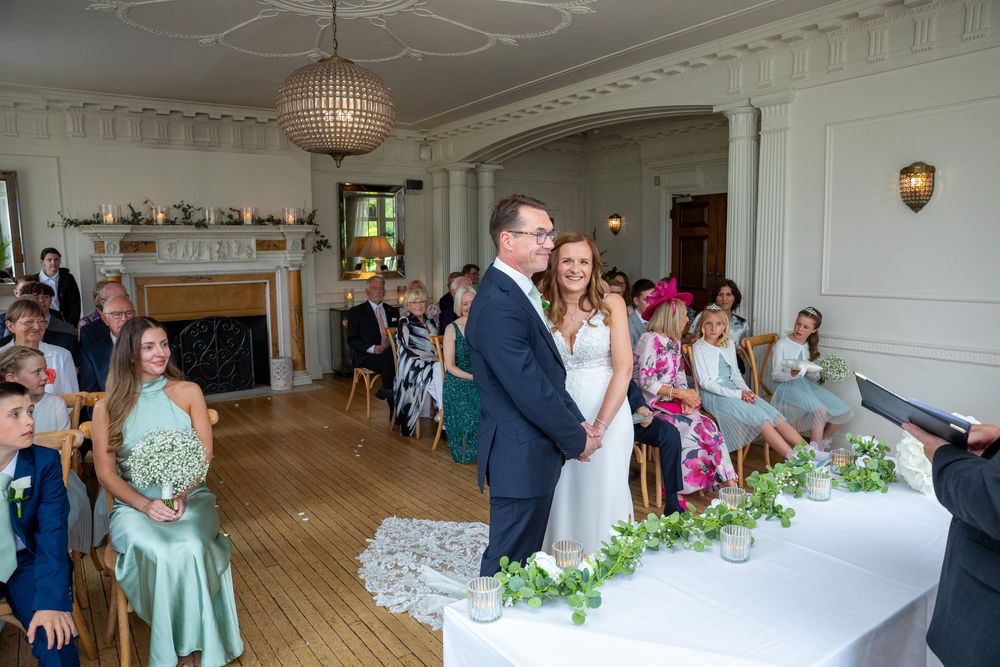 Bride and groom stand at the altar during an elegant indoor wedding ceremony in a grand white room.