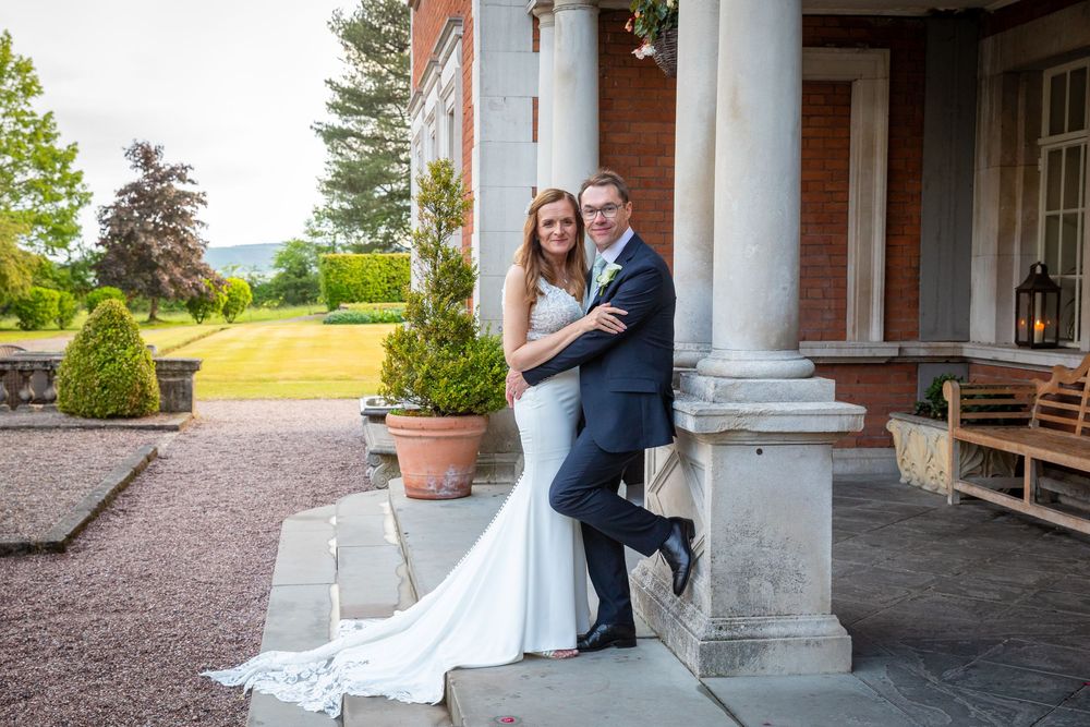 Bride and groom pose together on the steps of a grand country house wedding venue with scenic views.