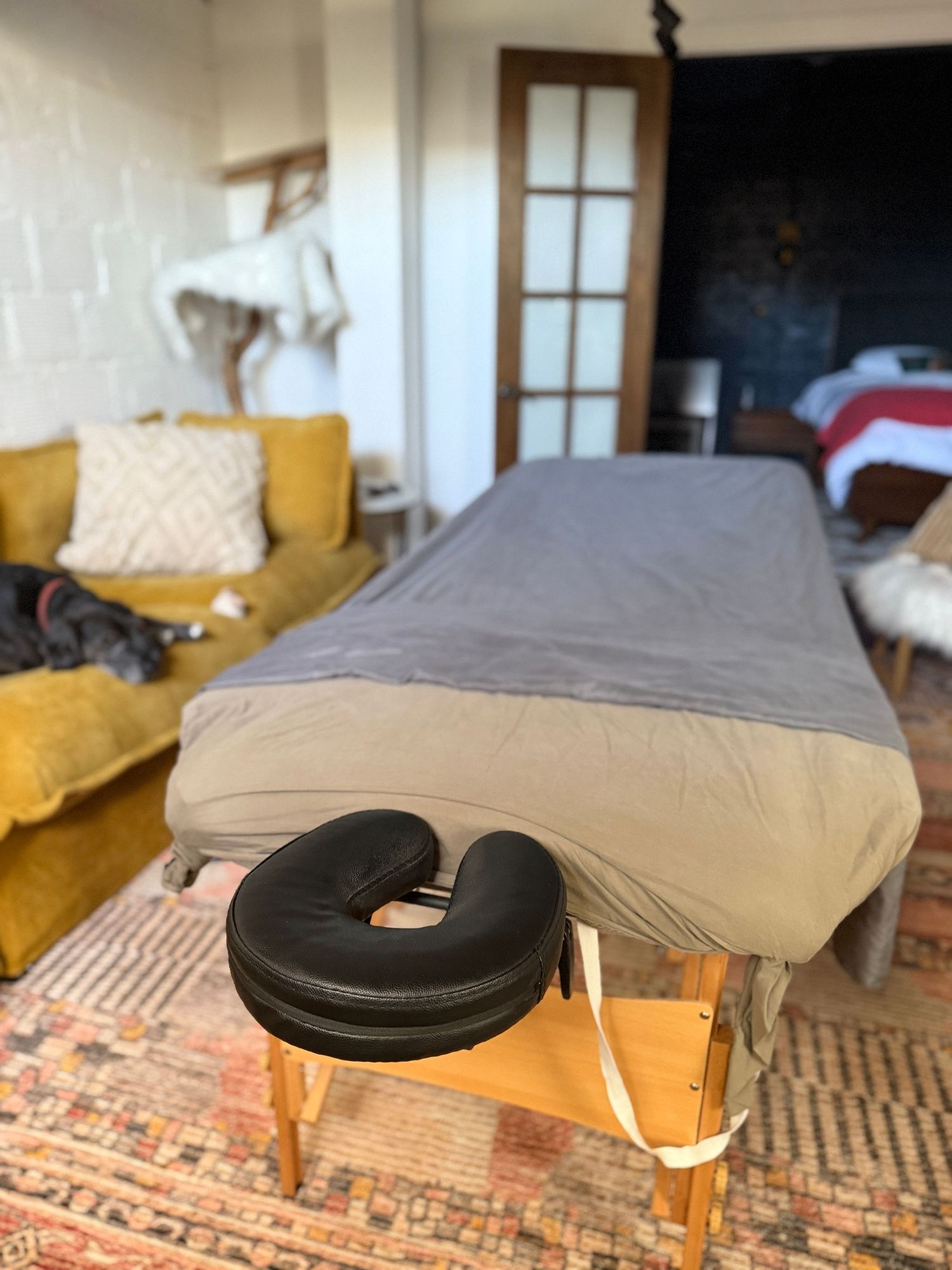 A portable massage table with black face cushion sits in a room with yellow chairs and a patterned rug.
