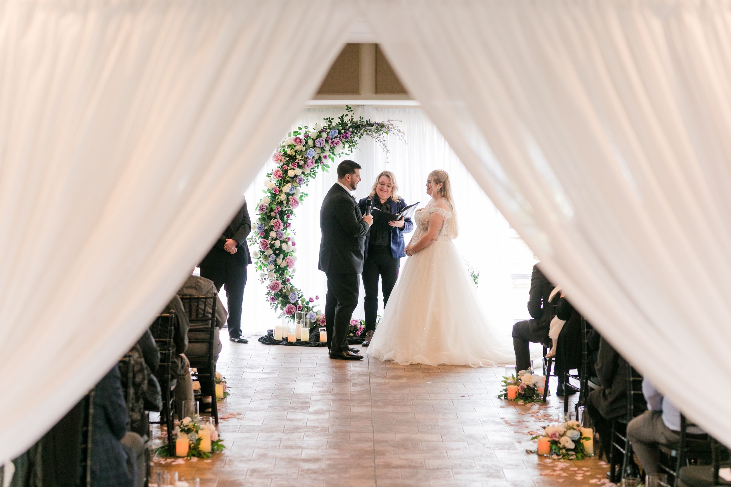 A panoramic view of an elegant indoor wedding ceremony with white drapes and floral arrangements.