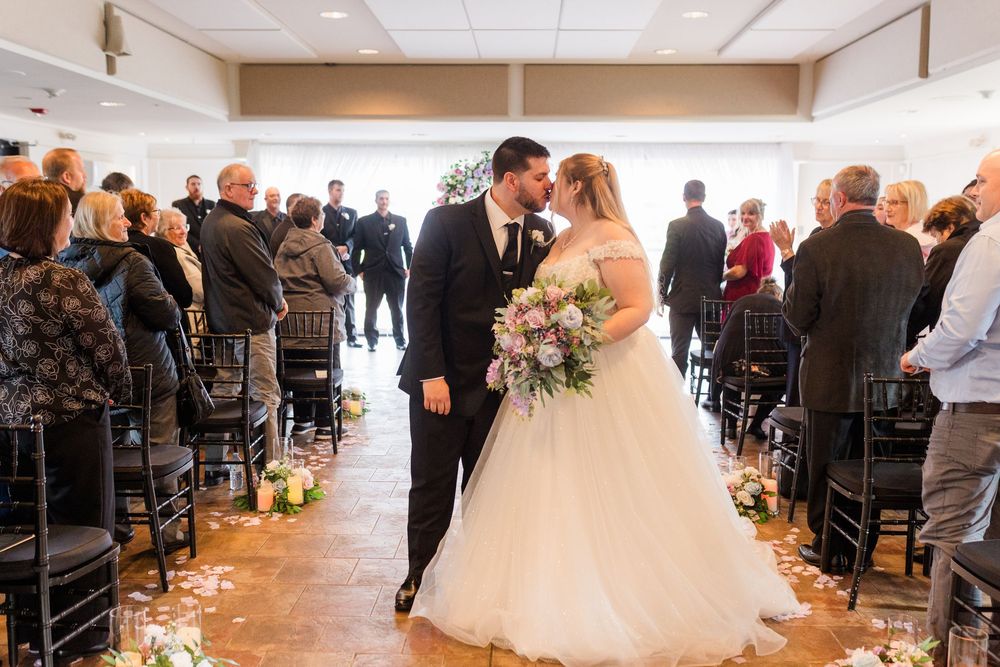 A panoramic view of an elegant indoor wedding ceremony with guests seated in rows of black chairs.