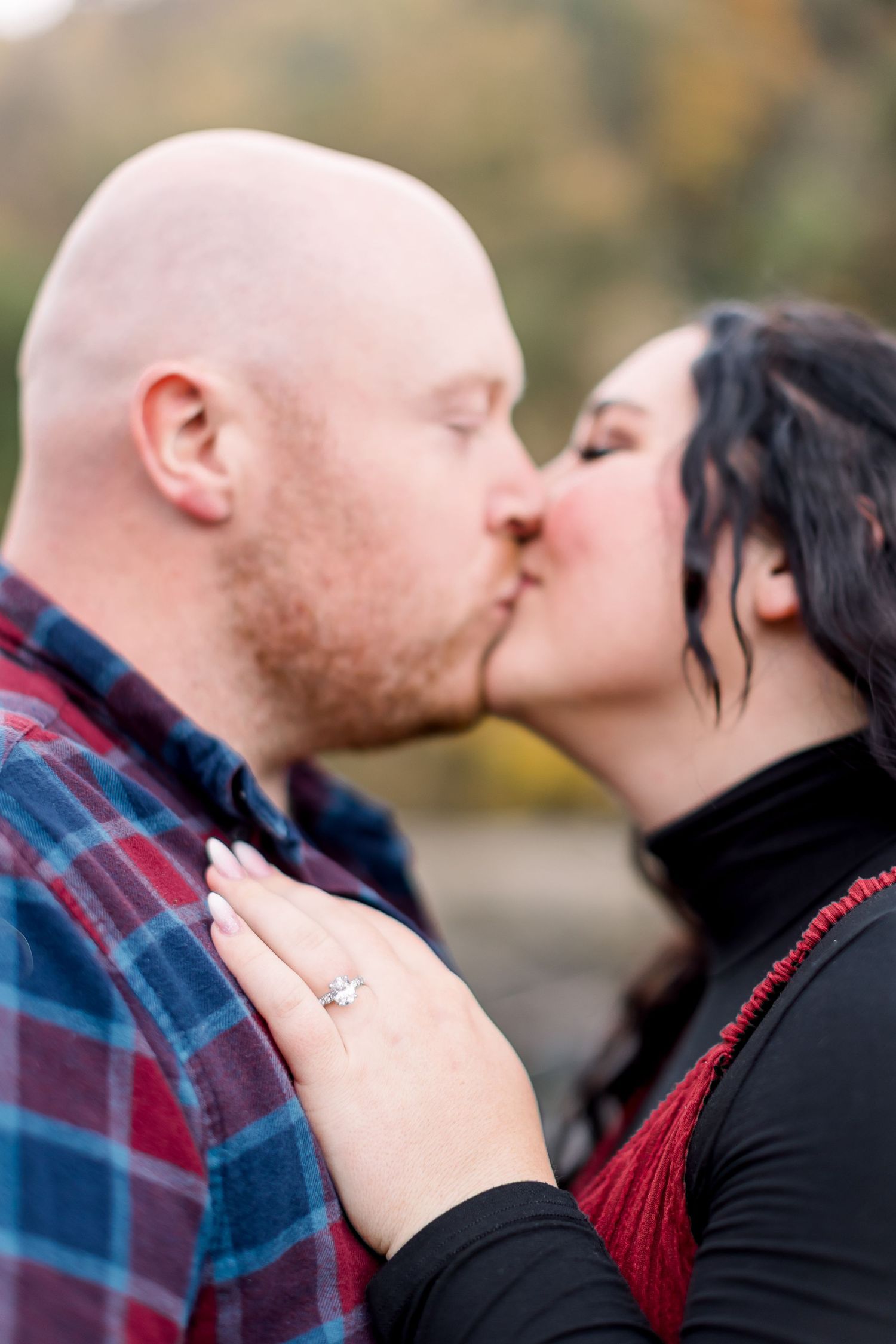 A romantic couple in plaid and black sharing intimate kisses in a photo outdoors.