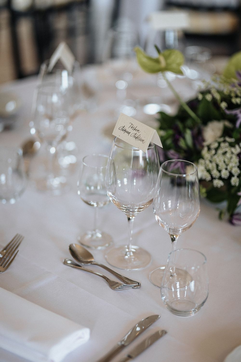 Elegant table settings with wine glasses, silverware and white tablecloths at a formal dining event.