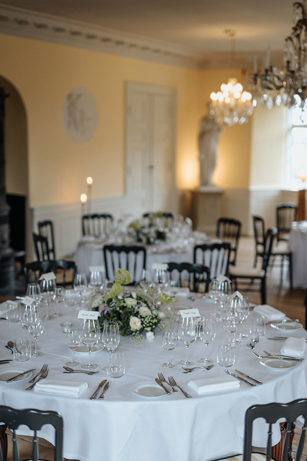 Elegant round dining tables with white linens, crystal glasses and floral centerpieces set for a formal banquet.