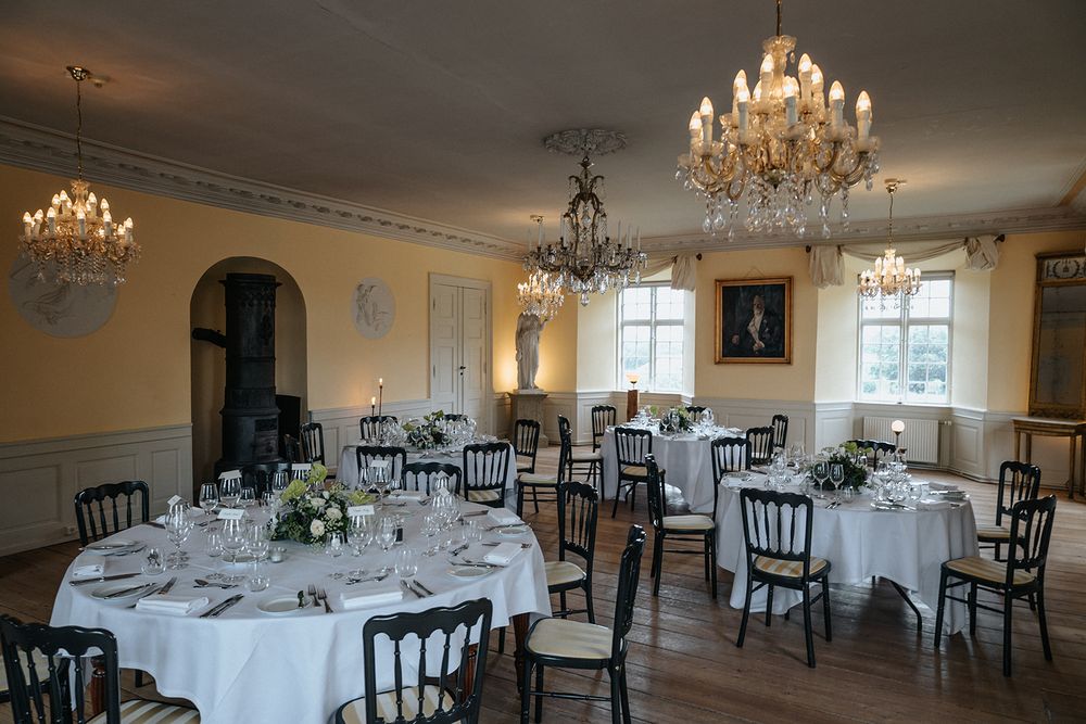 Elegant banquet hall with round tables, white linens, crystal chandeliers and dark chiavari chairs set for formal dining.
