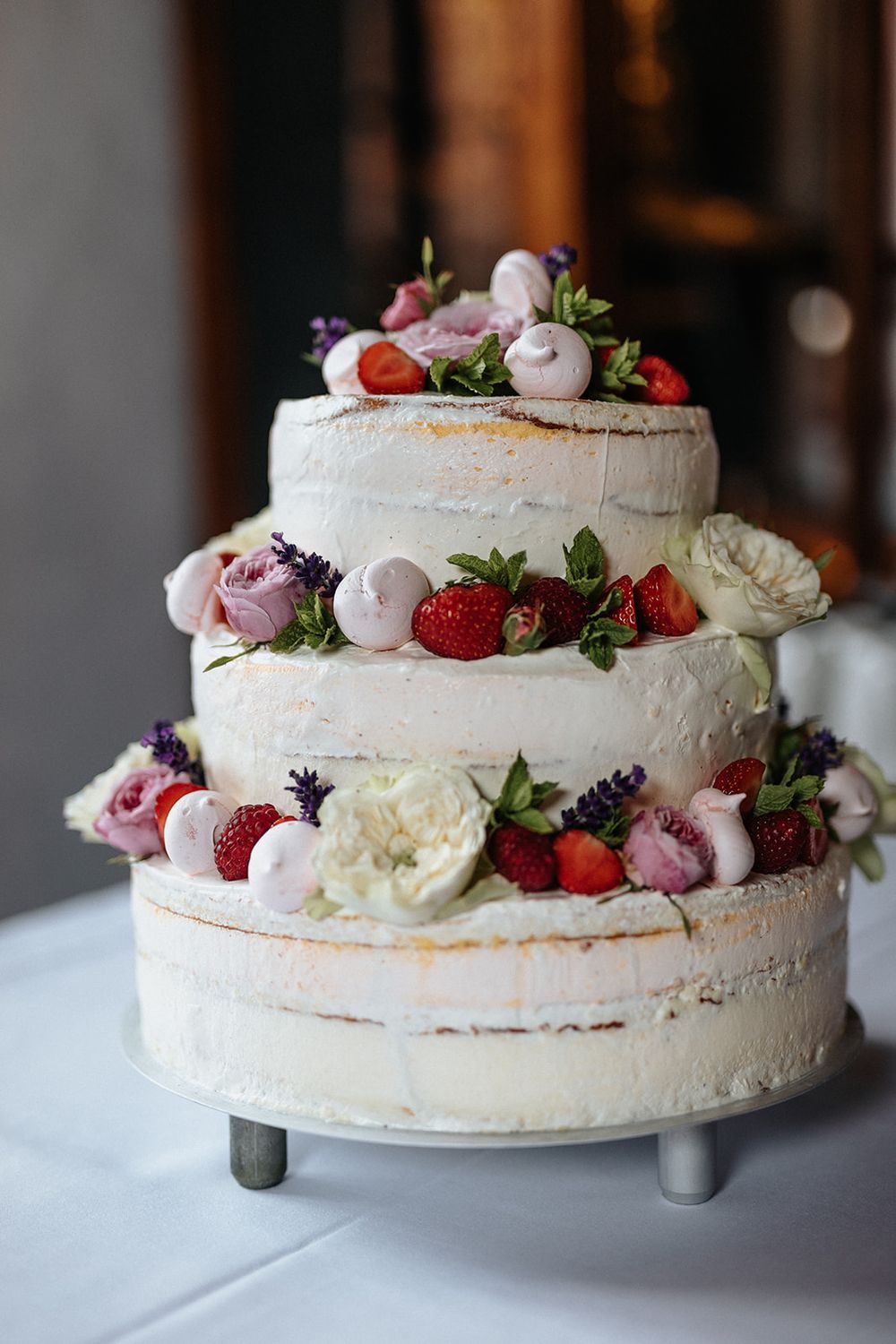 Elegant white pavlova cake decorated with fresh strawberries, pink macarons, and lavender flowers on a white cake stand.